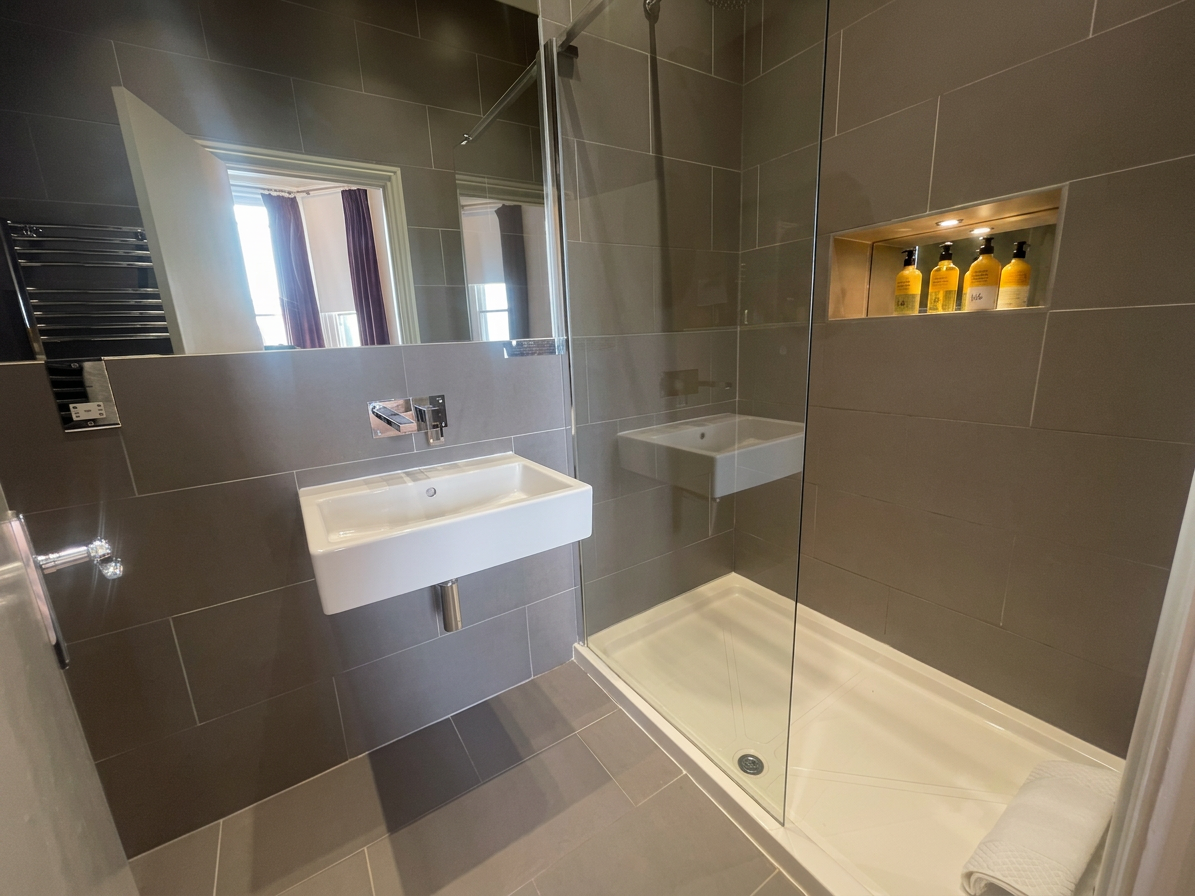 Hastings House Bedroom 3 ensuite — dark grey tiles, wall-hung basin, walk-in shower and Wild England toiletries