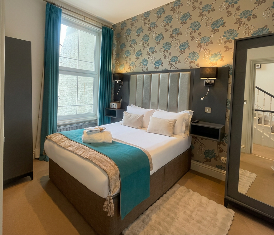 Hastings House Bedroom 2 — teal floral wallpaper, tall silver headboard