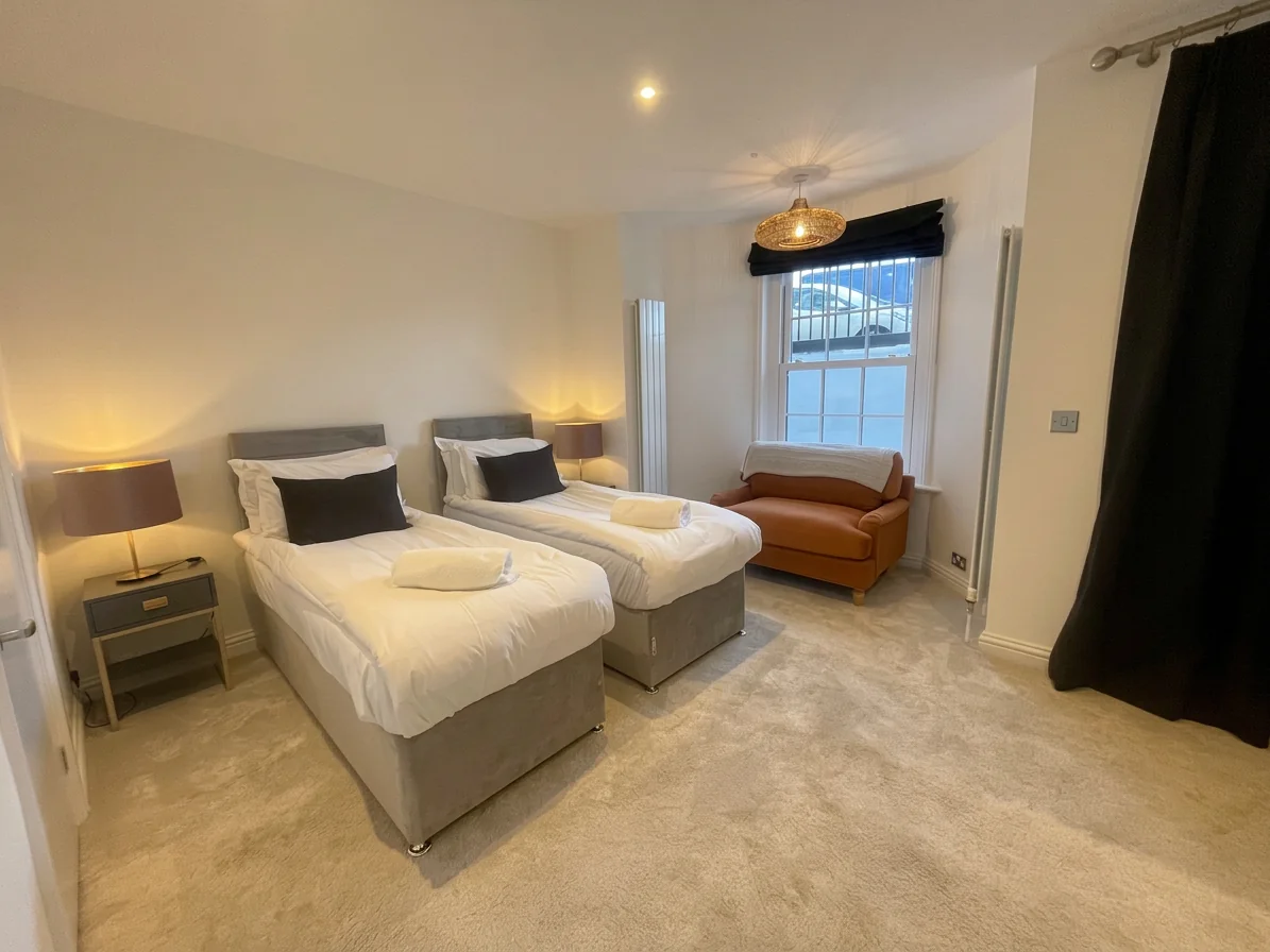Hastings House Bedroom 8 — twin beds with warm pendant light, leather armchair and wicker lamp
